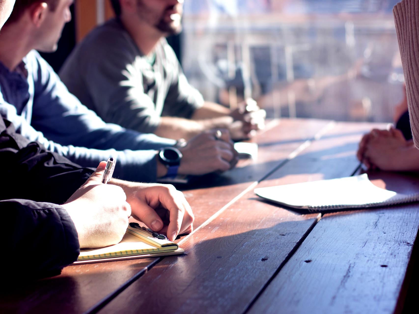 people sitting on chair in front of table while holding pens during daytime